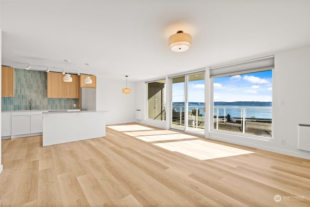 unfurnished living room featuring sink, rail lighting, light hardwood / wood-style flooring, radiator, and a water view