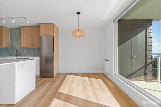 kitchen featuring pendant lighting, backsplash, plenty of natural light, and stainless steel refrigerator