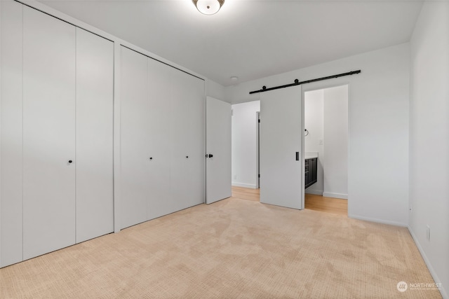 unfurnished bedroom featuring a barn door, ensuite bathroom, and light colored carpet