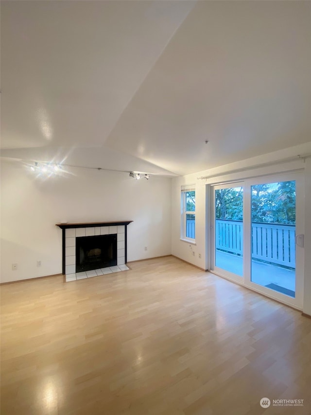 unfurnished living room featuring light hardwood / wood-style floors, vaulted ceiling, and a tiled fireplace