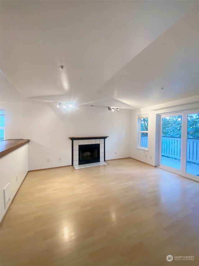 unfurnished living room featuring light wood-type flooring, vaulted ceiling, and a tile fireplace