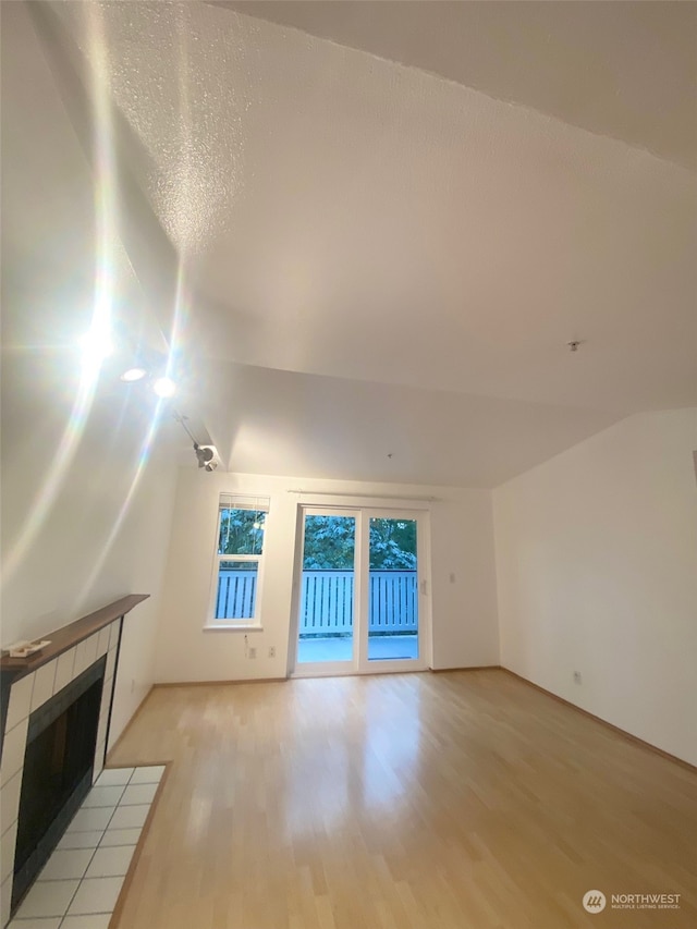 unfurnished living room featuring vaulted ceiling, light hardwood / wood-style floors, and a tile fireplace