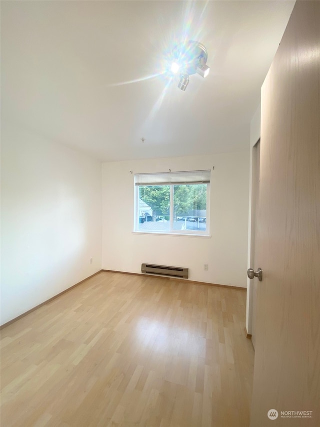 unfurnished room featuring baseboard heating and light hardwood / wood-style flooring