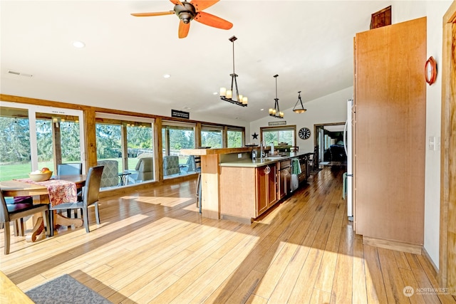 kitchen featuring hanging light fixtures, a center island with sink, light hardwood / wood-style flooring, ceiling fan with notable chandelier, and vaulted ceiling