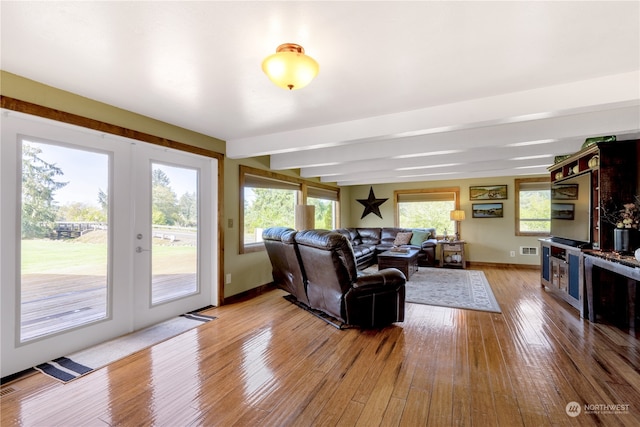 living room with light hardwood / wood-style flooring, a wealth of natural light, beamed ceiling, and french doors