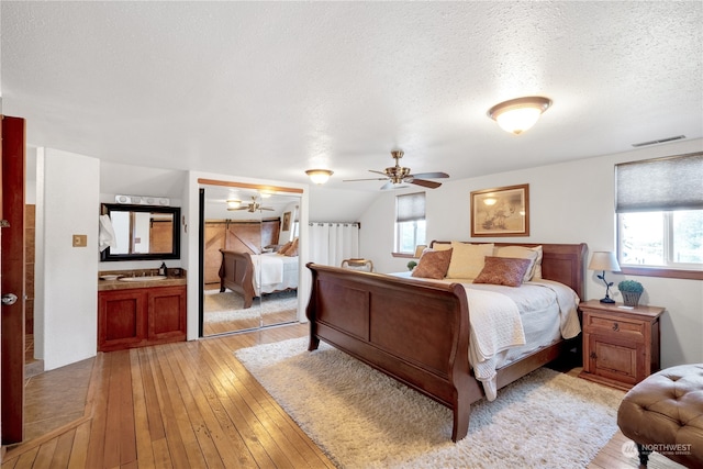 bedroom featuring ceiling fan, a textured ceiling, light hardwood / wood-style floors, and multiple windows