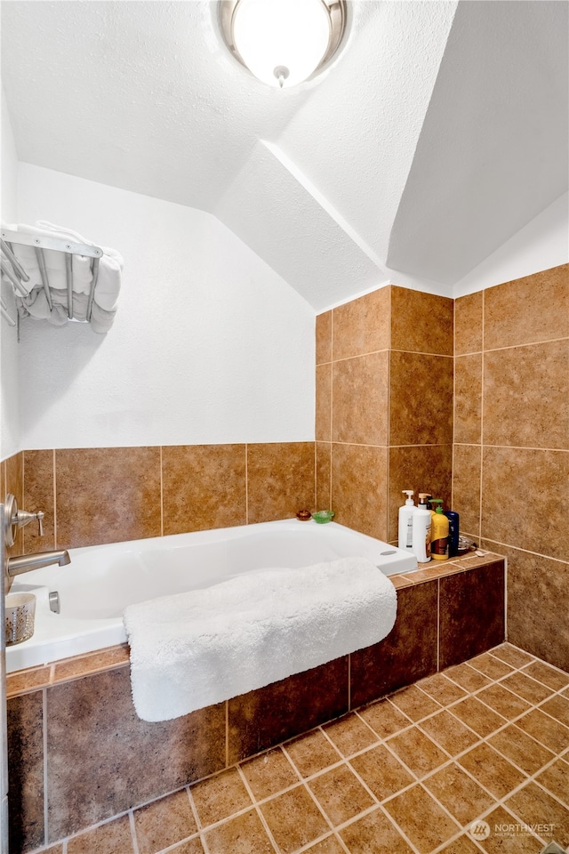 bathroom featuring lofted ceiling, a textured ceiling, tile patterned floors, tiled bath, and tile walls