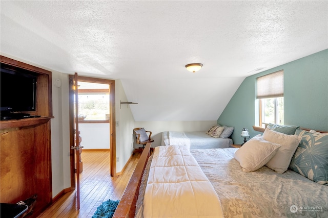 bedroom with a textured ceiling, lofted ceiling, and hardwood / wood-style flooring