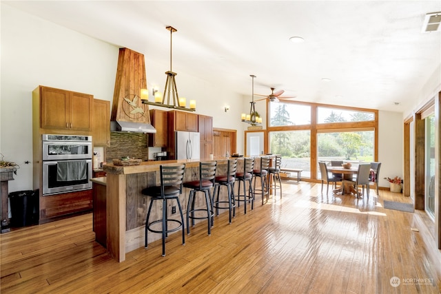 kitchen with appliances with stainless steel finishes, vaulted ceiling, ceiling fan with notable chandelier, light wood-type flooring, and decorative light fixtures