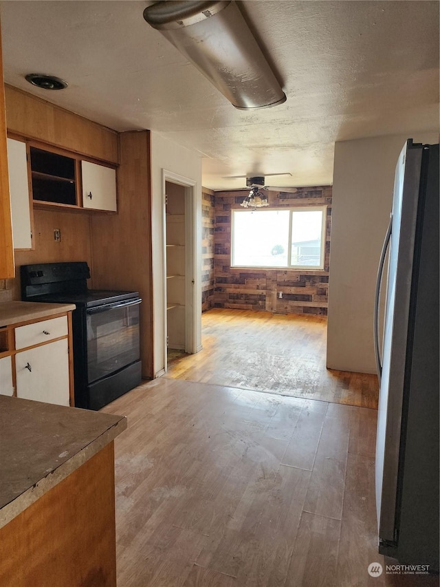 kitchen with white cabinetry, light wood-style floors, black / electric stove, and freestanding refrigerator