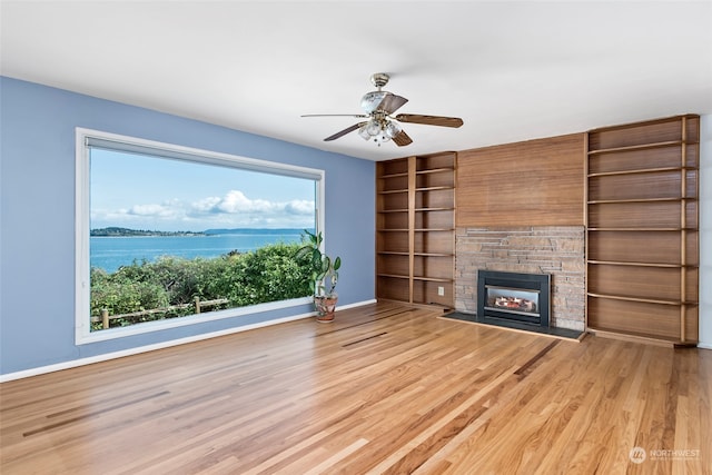 3224 SW Scenic Heights St, Oak Harbor, WA 98277 - unfurnished living room with wood finished floors, baseboards, ceiling fan, a stone fireplace, and a water view