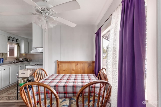 dining area with wood walls, ceiling fan, hardwood / wood-style flooring, and sink