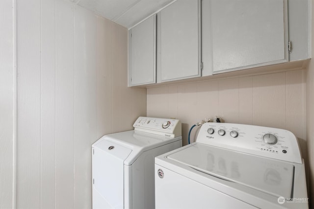 washroom with washer and clothes dryer, cabinets, and wooden walls