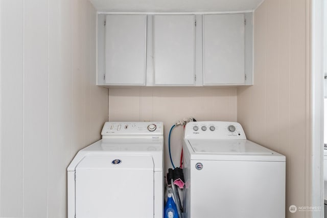 laundry room featuring cabinets, wooden walls, and separate washer and dryer