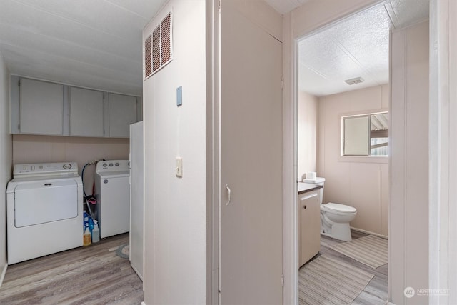 laundry area with light hardwood / wood-style flooring, cabinets, and separate washer and dryer