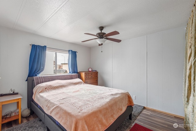 bedroom with ceiling fan, a textured ceiling, wooden walls, and hardwood / wood-style floors