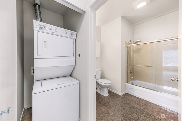 bathroom featuring stacked washer and clothes dryer, combined bath / shower with glass door, and toilet