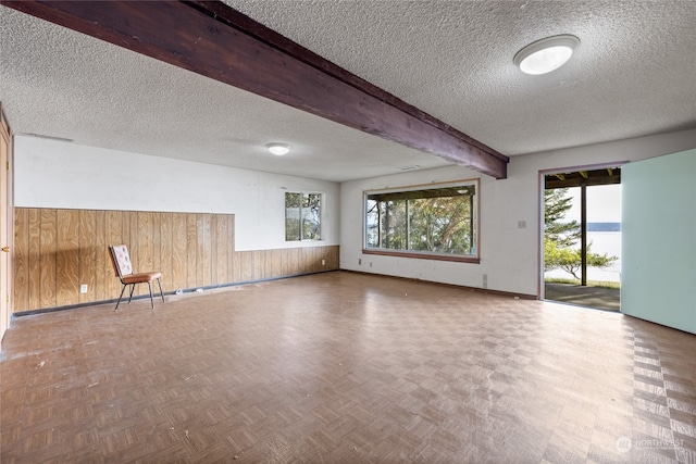 spare room with wooden walls, beam ceiling, a textured ceiling, and parquet floors