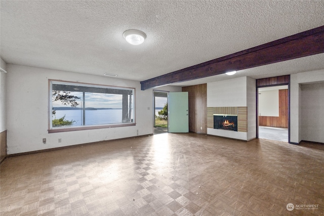 unfurnished living room with a textured ceiling, light parquet flooring, beam ceiling, and a brick fireplace