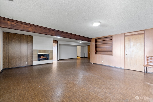 unfurnished living room with a textured ceiling, parquet floors, built in shelves, and wooden walls