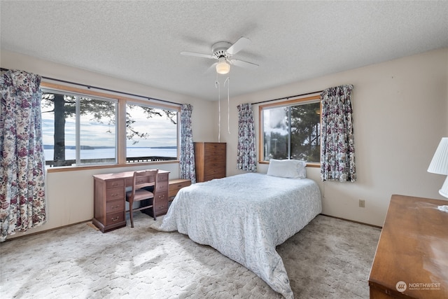 bedroom with ceiling fan, a textured ceiling, light carpet, and a water view