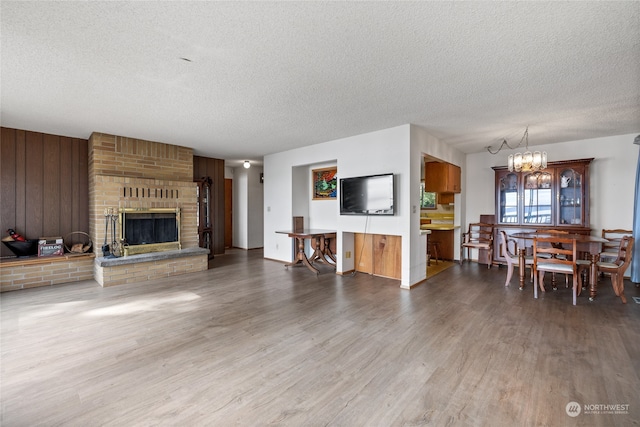 living room featuring an inviting chandelier, wood-type flooring, a textured ceiling, and a fireplace