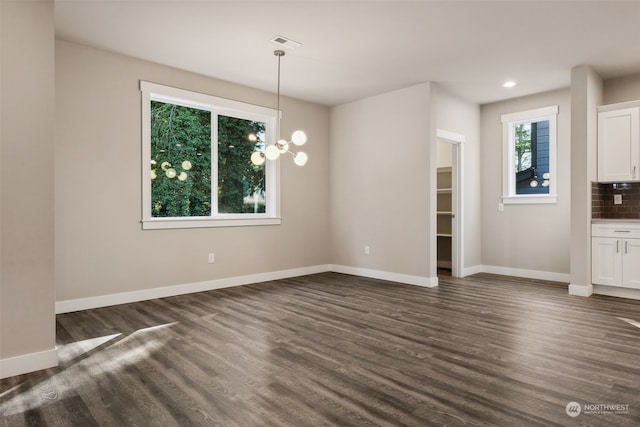 unfurnished dining area with an inviting chandelier, plenty of natural light, and dark wood-type flooring