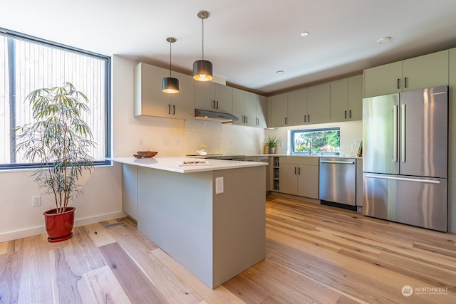 kitchen with pendant lighting, sink, kitchen peninsula, appliances with stainless steel finishes, and light hardwood / wood-style floors