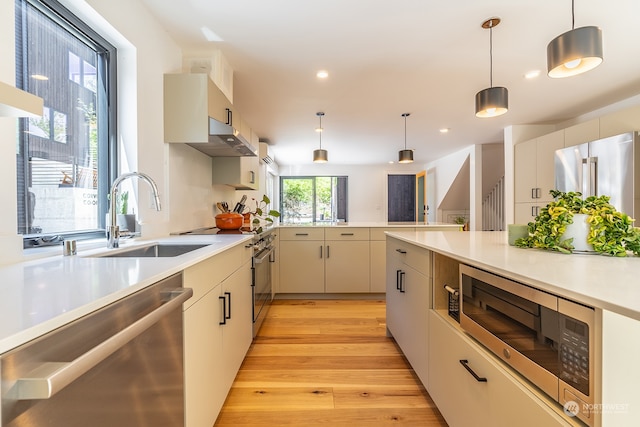 kitchen featuring kitchen peninsula, pendant lighting, stainless steel appliances, light hardwood / wood-style flooring, and sink