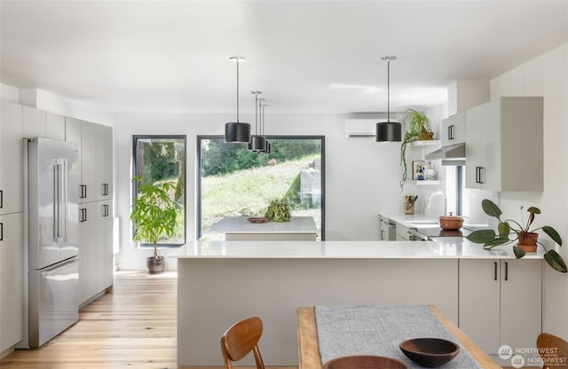 kitchen featuring hanging light fixtures, light hardwood / wood-style floors, stainless steel refrigerator, kitchen peninsula, and sink