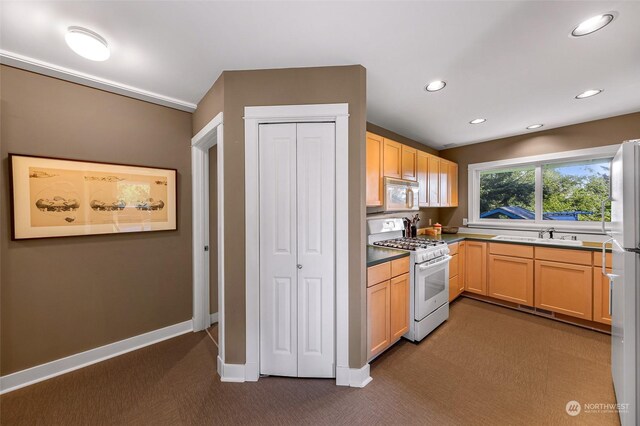 kitchen with light brown cabinetry, dark colored carpet, and white appliances