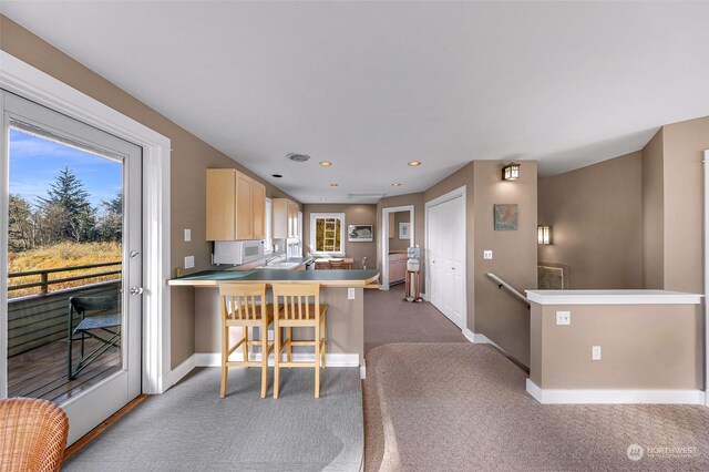 kitchen featuring dark colored carpet, kitchen peninsula, light brown cabinets, and a breakfast bar area