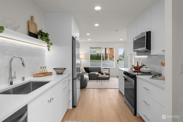 kitchen with stainless steel appliances, decorative backsplash, light hardwood / wood-style floors, sink, and white cabinetry