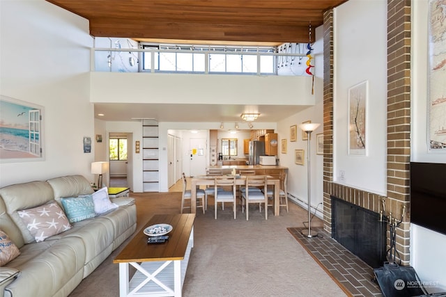 carpeted living room with a brick fireplace, a high ceiling, and wooden ceiling