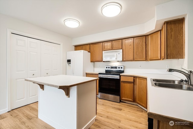 kitchen with sink, white appliances, a kitchen island, light hardwood / wood-style flooring, and a kitchen bar