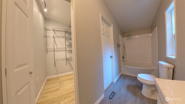 full bathroom with lofted ceiling, hardwood / wood-style floors, vanity, tiled shower / bath, and toilet