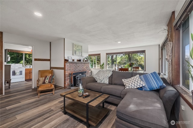 living room with a brick fireplace, a textured ceiling, and hardwood / wood-style flooring