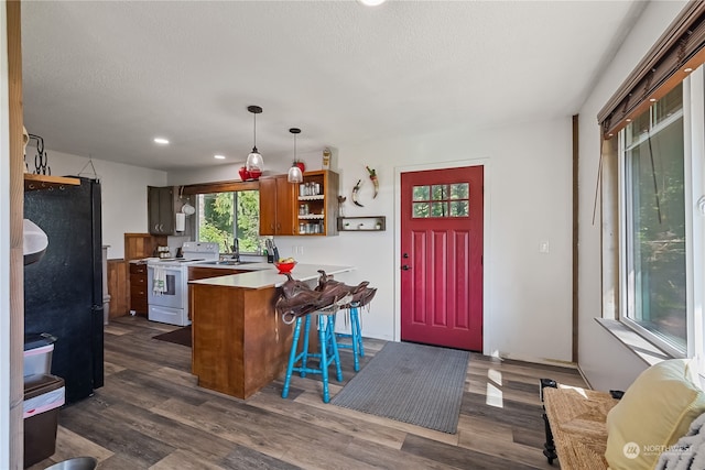 kitchen with hanging light fixtures, kitchen peninsula, a kitchen bar, white range with electric cooktop, and black refrigerator