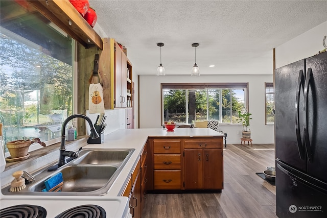 kitchen with hanging light fixtures, kitchen peninsula, black refrigerator, hardwood / wood-style floors, and sink