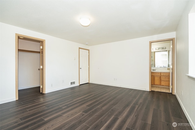 unfurnished bedroom with ensuite bath, a closet, and dark hardwood / wood-style flooring