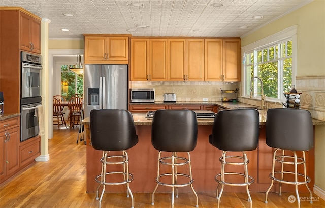 kitchen featuring light hardwood / wood-style floors, a kitchen bar, stainless steel appliances, crown molding, and dark stone countertops