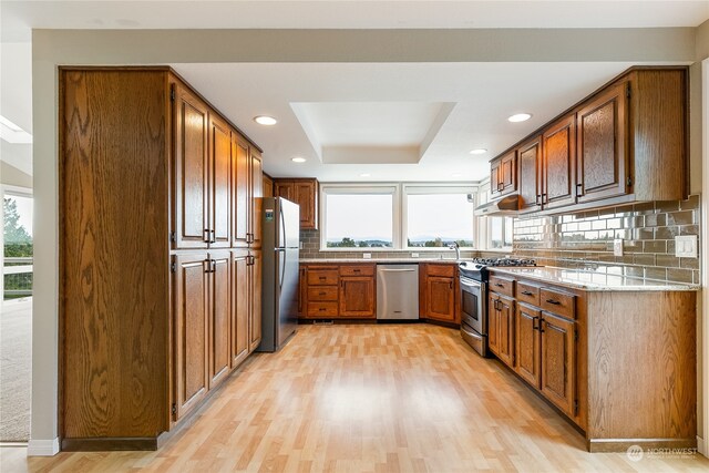 kitchen with appliances with stainless steel finishes, backsplash, a raised ceiling, and light hardwood / wood-style flooring