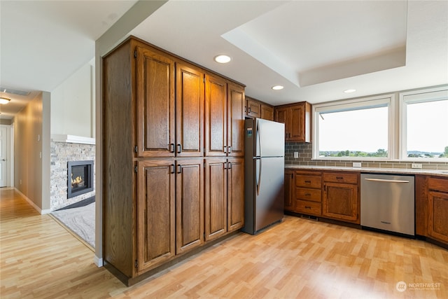 kitchen featuring a stone fireplace, appliances with stainless steel finishes, light wood-type flooring, and a raised ceiling