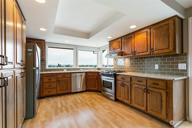 kitchen with a tray ceiling, light hardwood / wood-style floors, sink, decorative backsplash, and appliances with stainless steel finishes