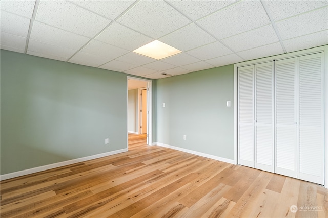 unfurnished bedroom with light wood-type flooring, a drop ceiling, and a closet