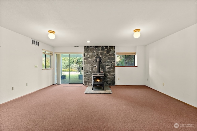 unfurnished living room with carpet flooring, a wood stove, and a healthy amount of sunlight