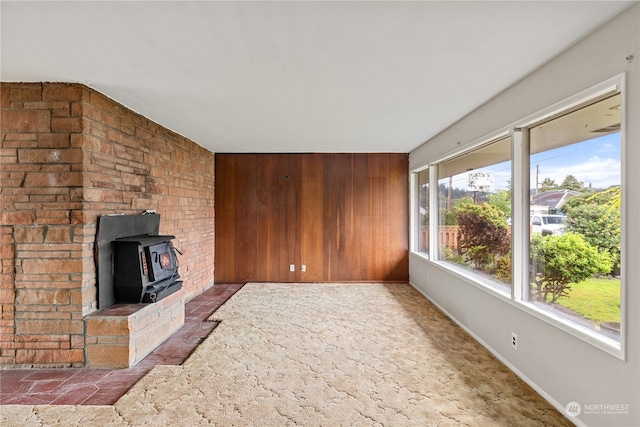 unfurnished living room with dark carpet, wooden walls, and a wood stove