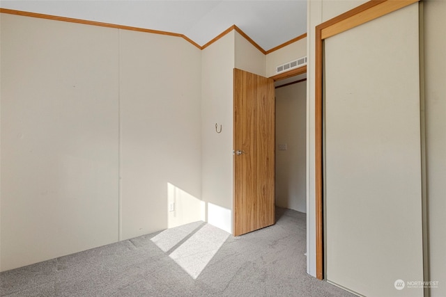 unfurnished bedroom featuring light carpet, lofted ceiling, crown molding, and a closet