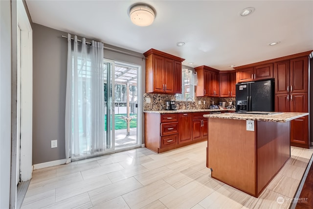 kitchen featuring a center island, tasteful backsplash, sink, light stone countertops, and black refrigerator with ice dispenser