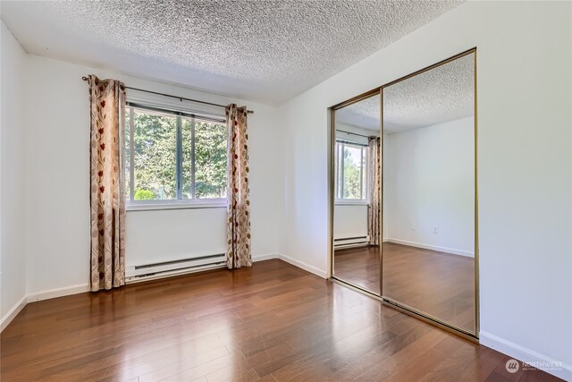 unfurnished bedroom featuring a textured ceiling, dark hardwood / wood-style floors, a baseboard heating unit, and a closet